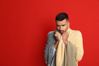 Man wrapped in warm blanket suffering from cold on red background, space for text