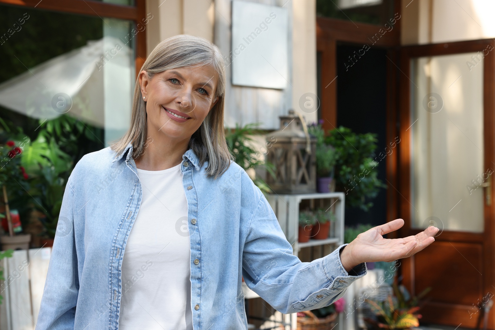 Photo of Happy business owner inviting to come into her flower shop outdoors