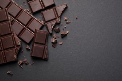 Photo of Pieces of delicious dark chocolate bars on black background, flat lay. Space for text
