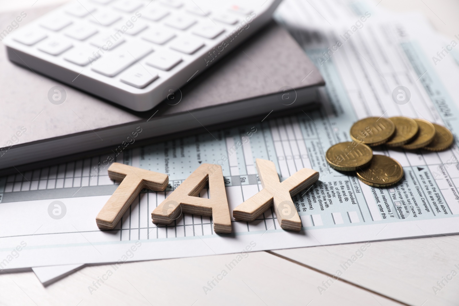 Photo of Word Tax made with letters, calculator, document, notebook and coins on white wooden table, closeup