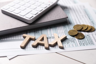 Photo of Word Tax made with letters, calculator, document, notebook and coins on white wooden table, closeup