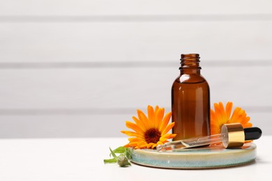 Bottle of essential oil and beautiful calendula flowers on white table, space for text
