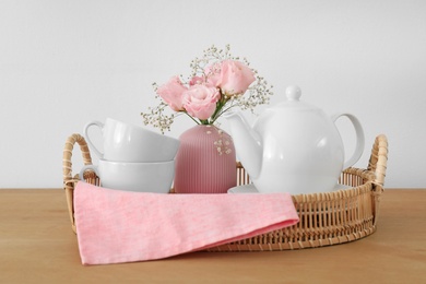 Tray with ceramic tea set and beautiful bouquet on wooden table