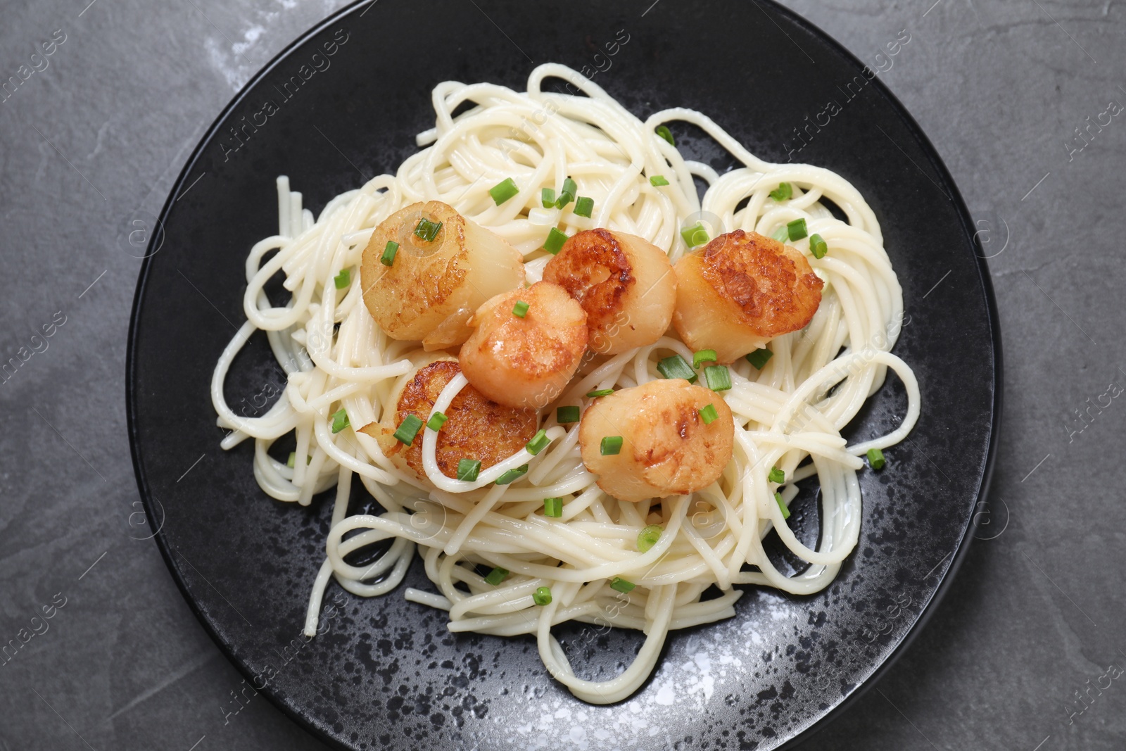 Photo of Delicious scallop pasta with green onion on grey table, top view