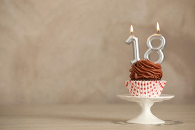 Photo of 18th birthday, coming of age party. Delicious cupcake with number shaped candles on beige table, space for text