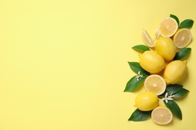 Many fresh ripe lemons with green leaves and flowers on yellow background, flat lay. Space for text