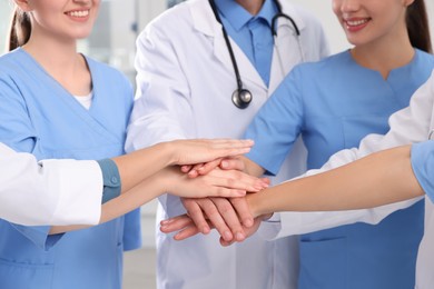 Photo of Teammedical doctors putting hands together indoors, closeup