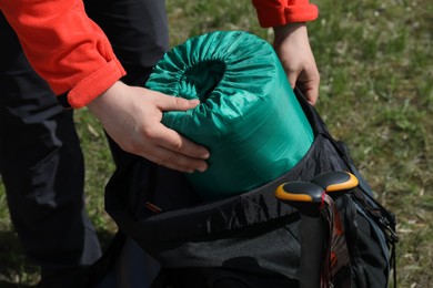 Photo of Hiker putting sleeping bag into backpack outdoors, closeup