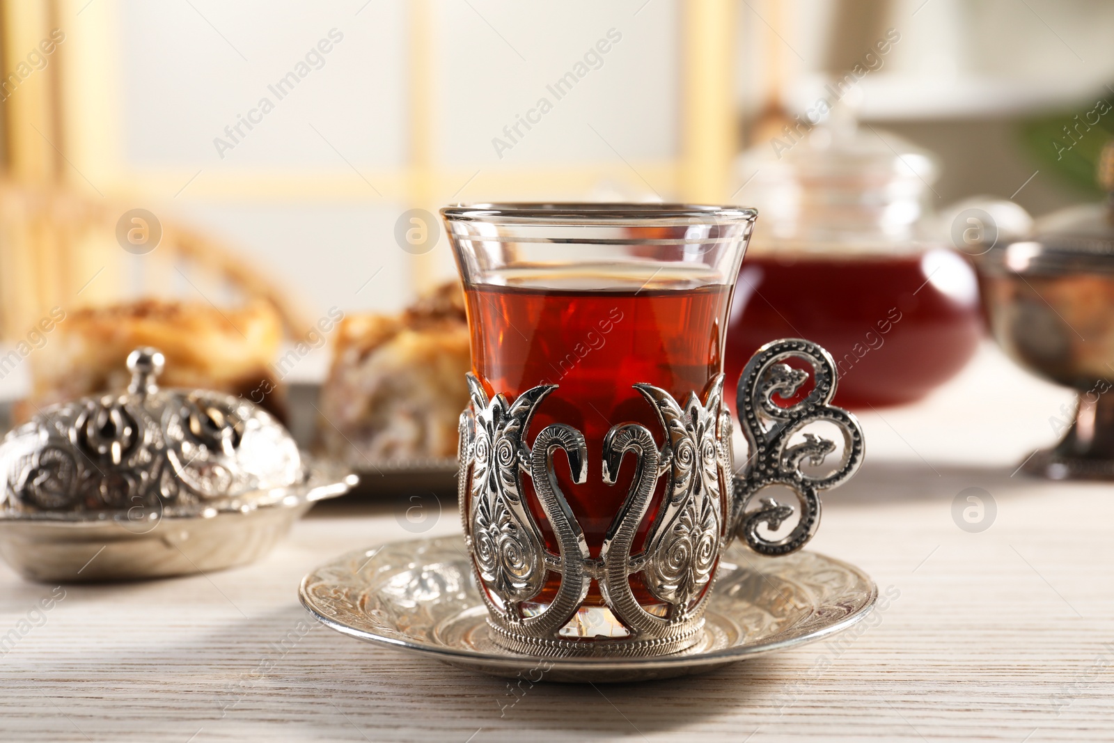 Photo of Glass of traditional Turkish tea in vintage holder on white wooden table