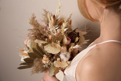 Photo of Bride holding beautiful dried flower bouquet on beige background, closeup