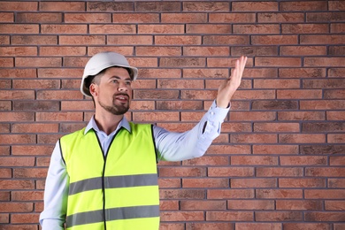 Photo of Male industrial engineer in uniform on brick wall background, space for text. Safety equipment
