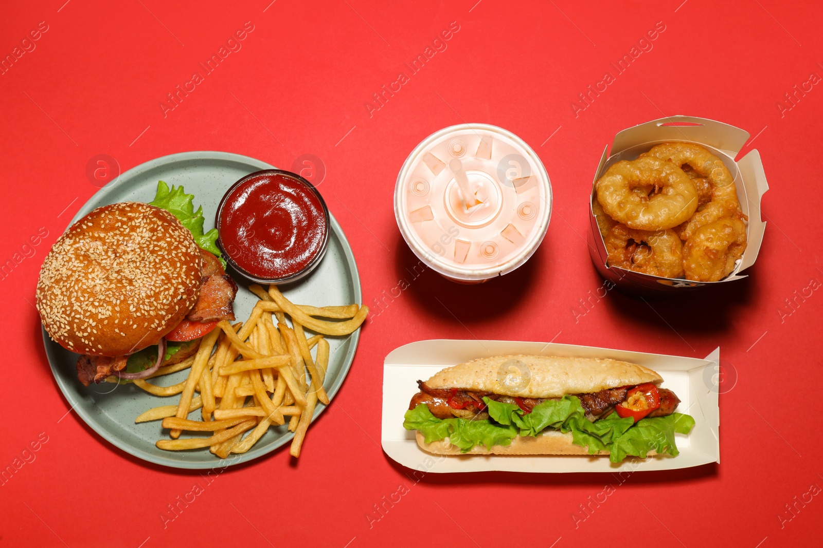 Photo of Tasty burger, French fries, hot dog, fried onion rings and refreshing drink on red background, flat lay. Fast food