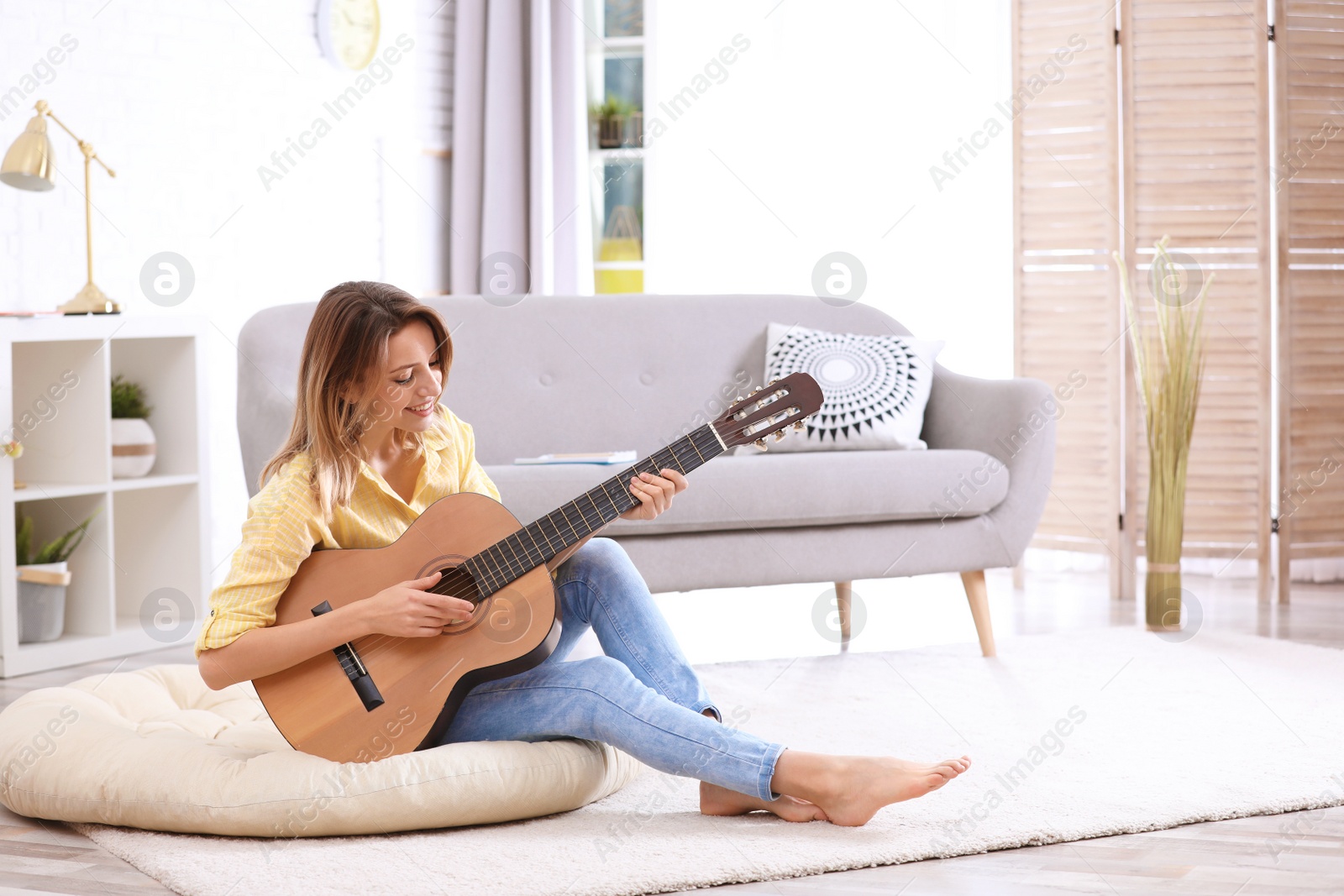 Photo of Young woman playing acoustic guitar in living room