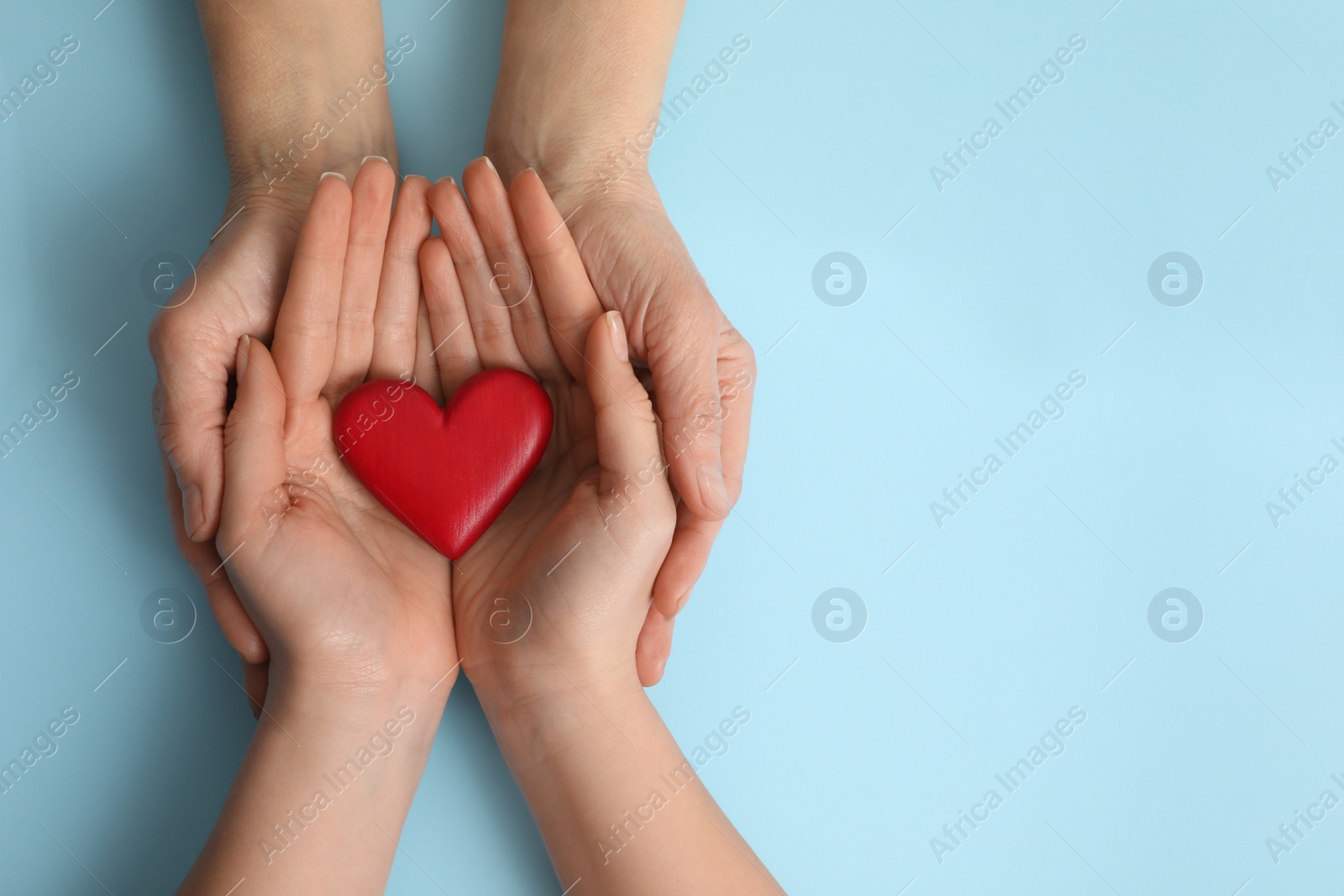 Photo of Young and elderly women holding red heart on light blue background, top view. Space for text