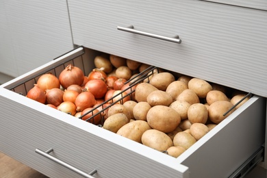 Photo of Open drawer with potatoes and onions in kitchen. Orderly storage