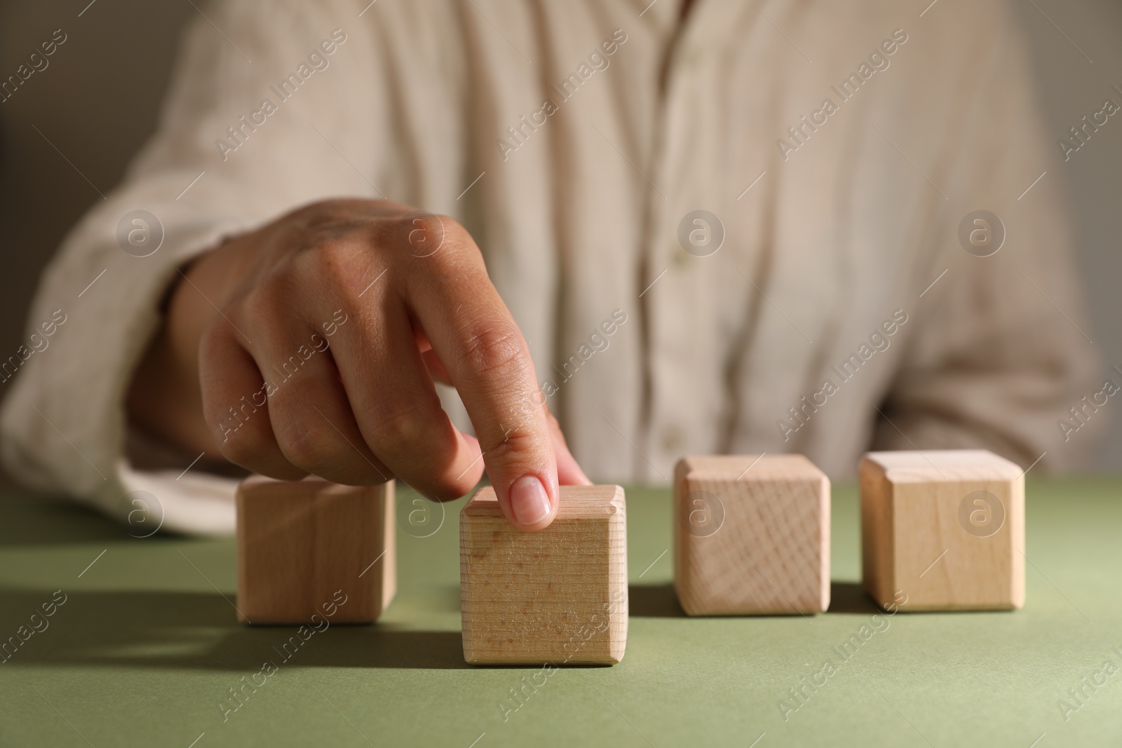 Photo of Woman choosing wooden cube among others at green table, closeup