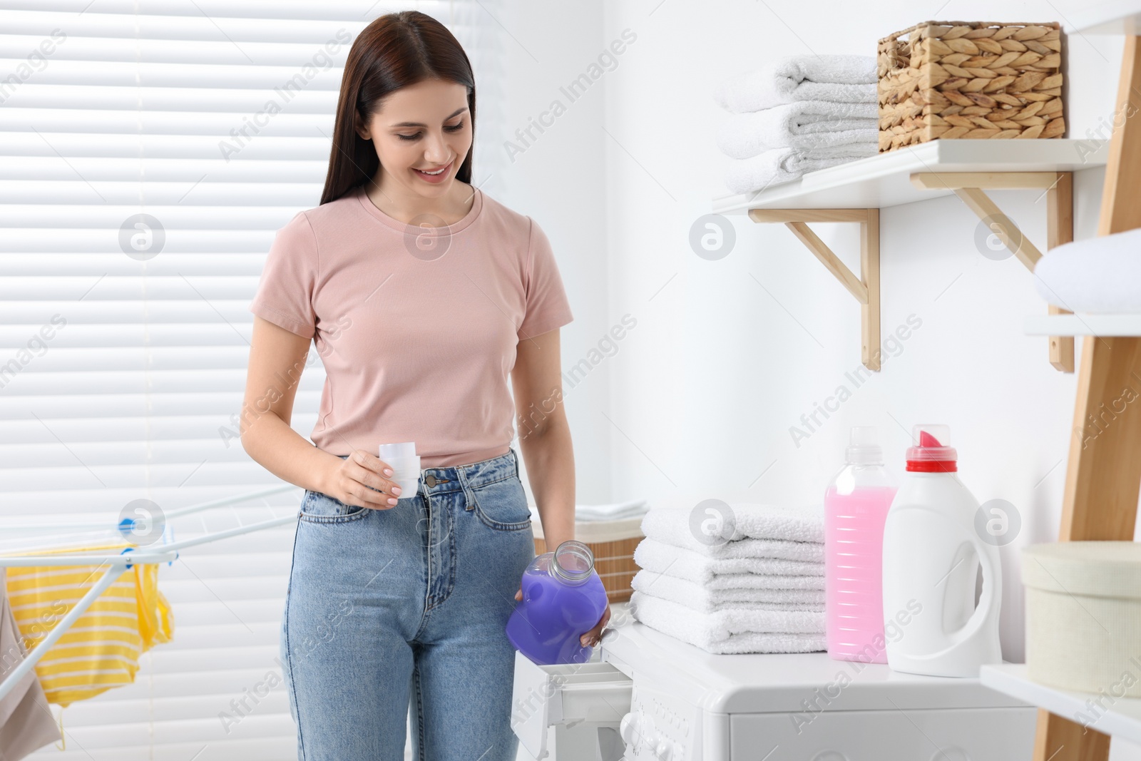 Photo of Woman pouring fabric softener into washing machine in bathroom, space for text