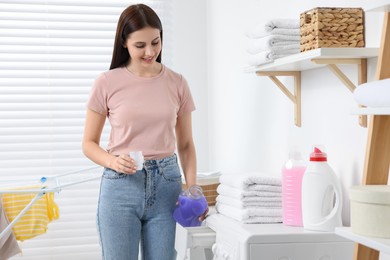 Woman pouring fabric softener into washing machine in bathroom, space for text