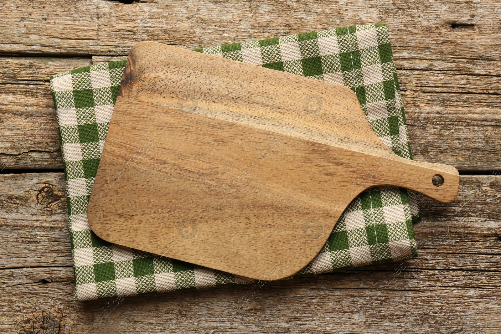 Photo of New cutting board and kitchen towel on old wooden table, top view