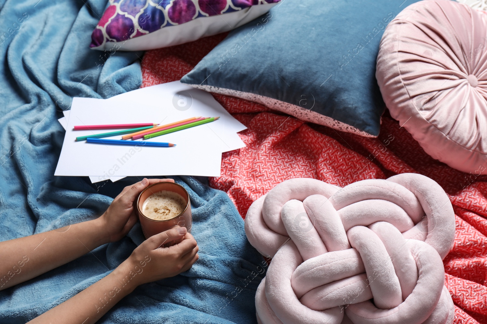 Photo of Woman holding cup of coffee while lying on bed with pillows and warm plaid, closeup