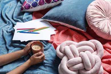 Photo of Woman holding cup of coffee while lying on bed with pillows and warm plaid, closeup