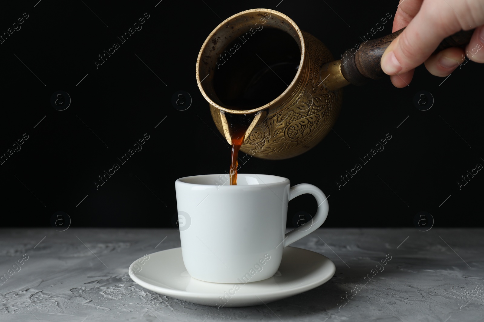 Photo of Turkish coffee. Woman pouring brewed beverage from cezve into cup at grey table, closeup