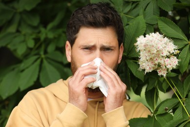 Man suffering from seasonal spring allergy near tree in park