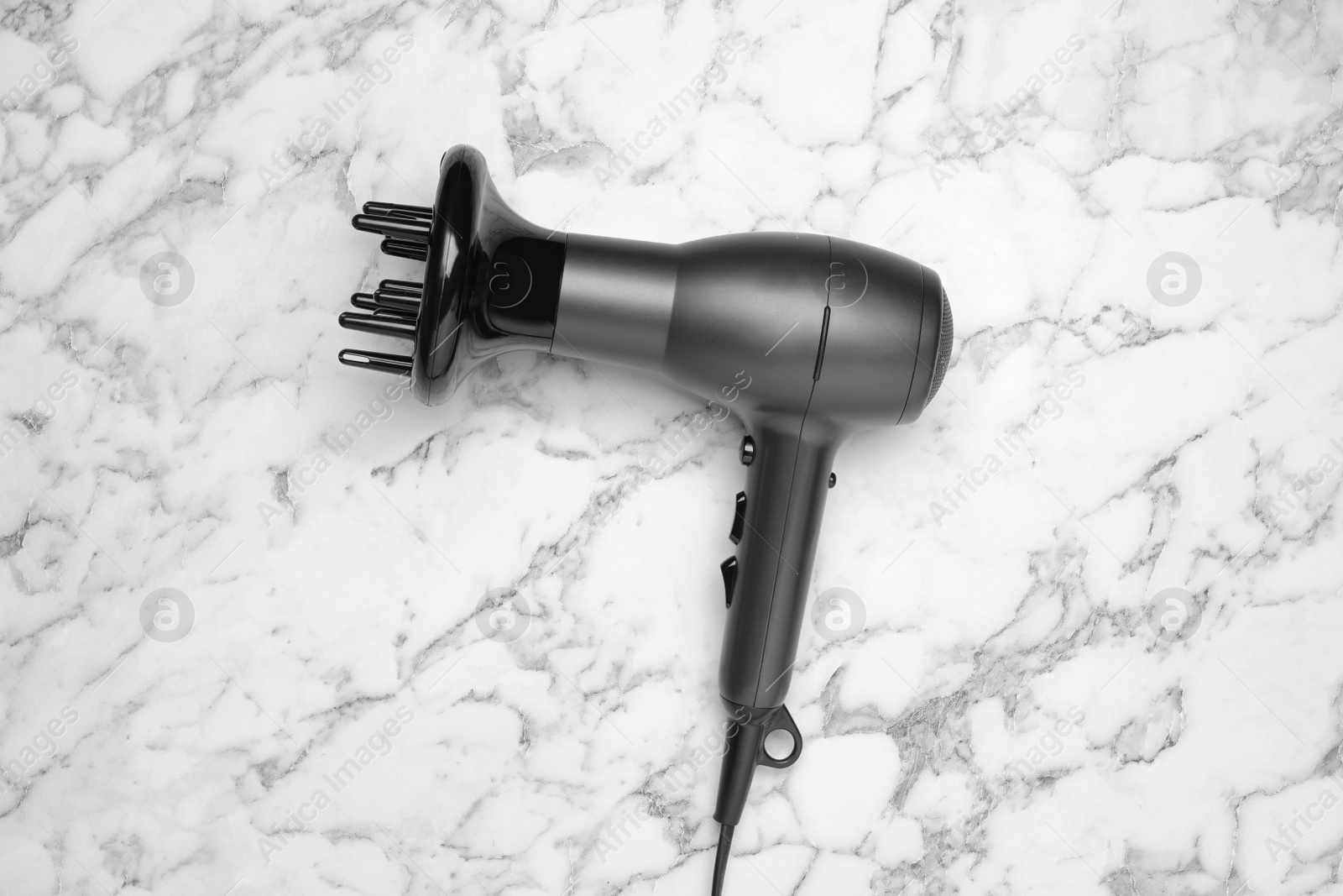 Photo of Hair dryer on white marble table, top view. Professional hairdresser tool