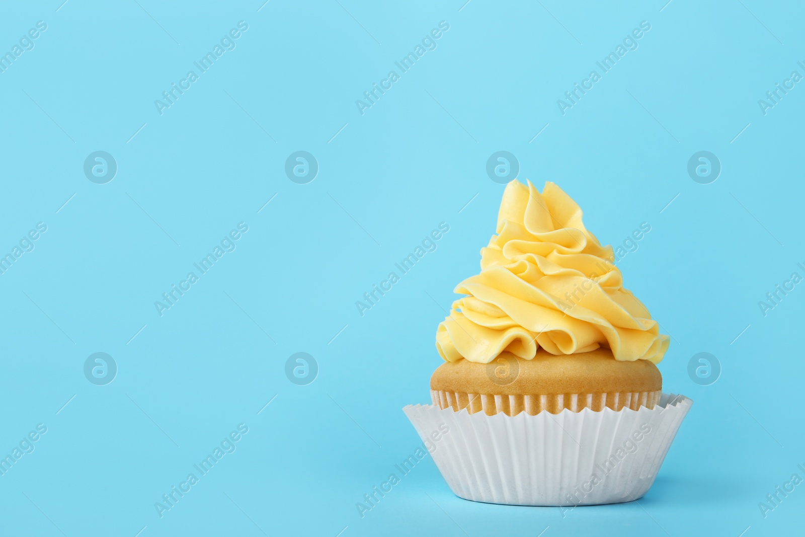 Photo of Tasty cupcake with cream on light blue background, space for text