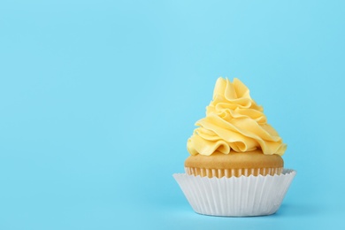 Photo of Tasty cupcake with cream on light blue background, space for text