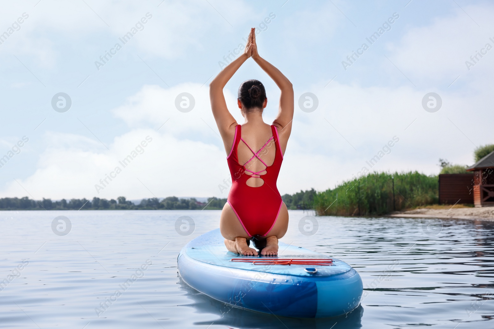 Photo of Woman practicing yoga on light blue SUP board on river, back view