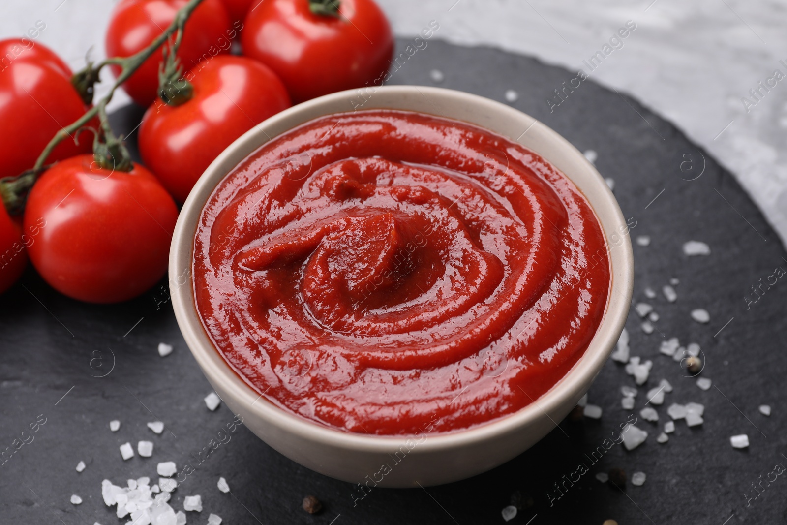 Photo of Organic ketchup in bowl, fresh tomatoes and spices on table, closeup. Tomato sauce