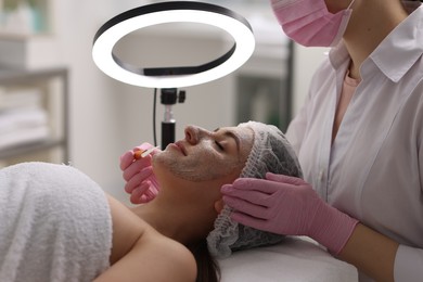 Photo of Cosmetologist applying mask on woman's face in clinic, closeup