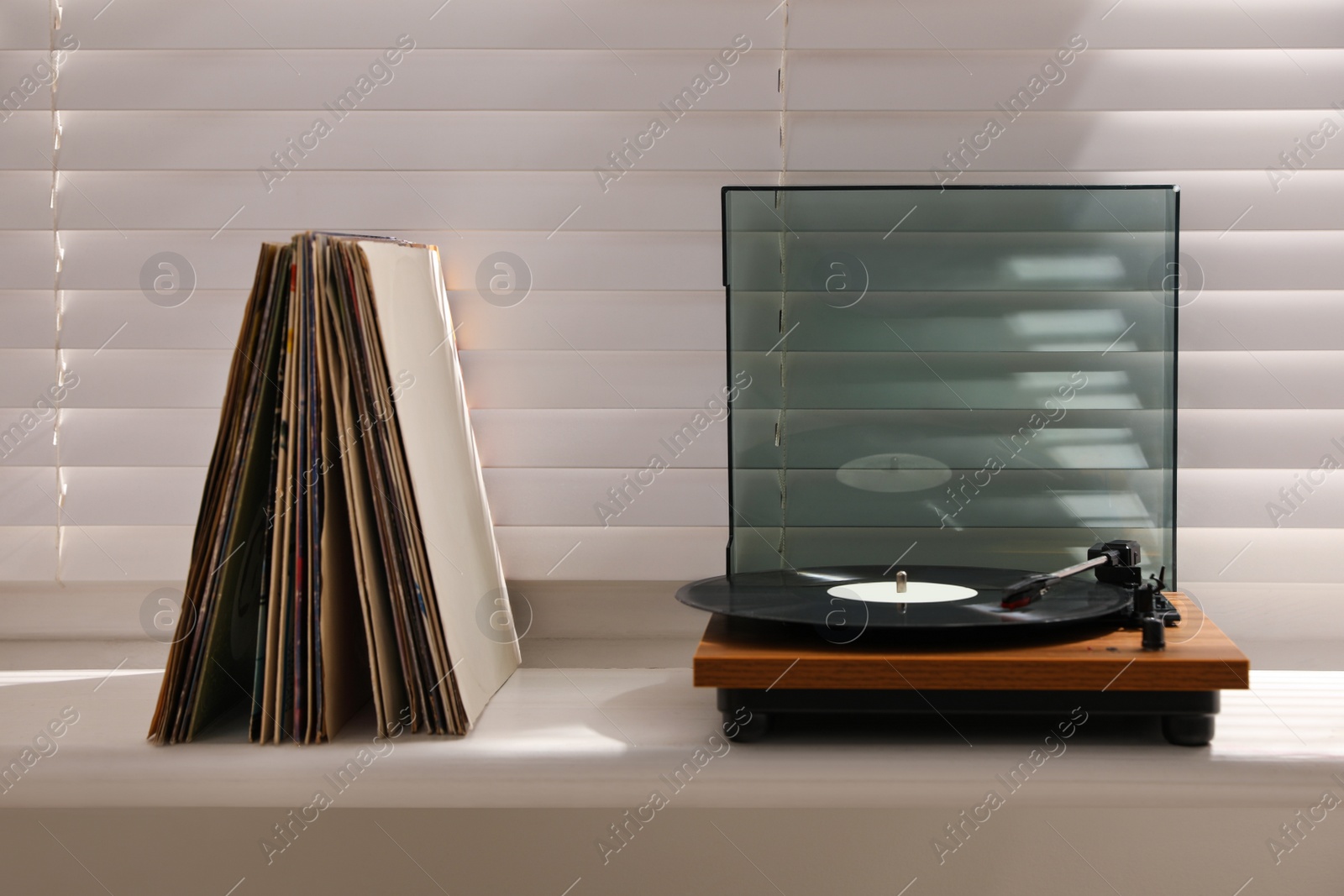 Photo of Stylish turntable with vinyl discs on windowsill in room