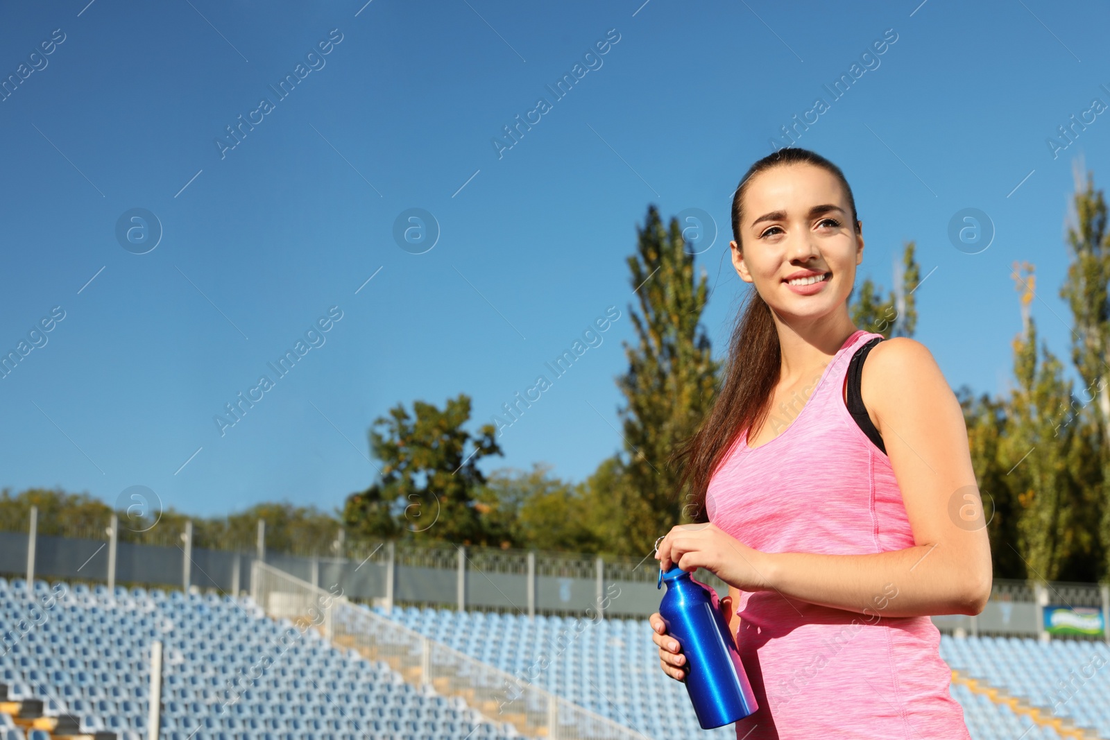 Photo of Sporty woman with bottle of water at stadium on sunny day. Space for text