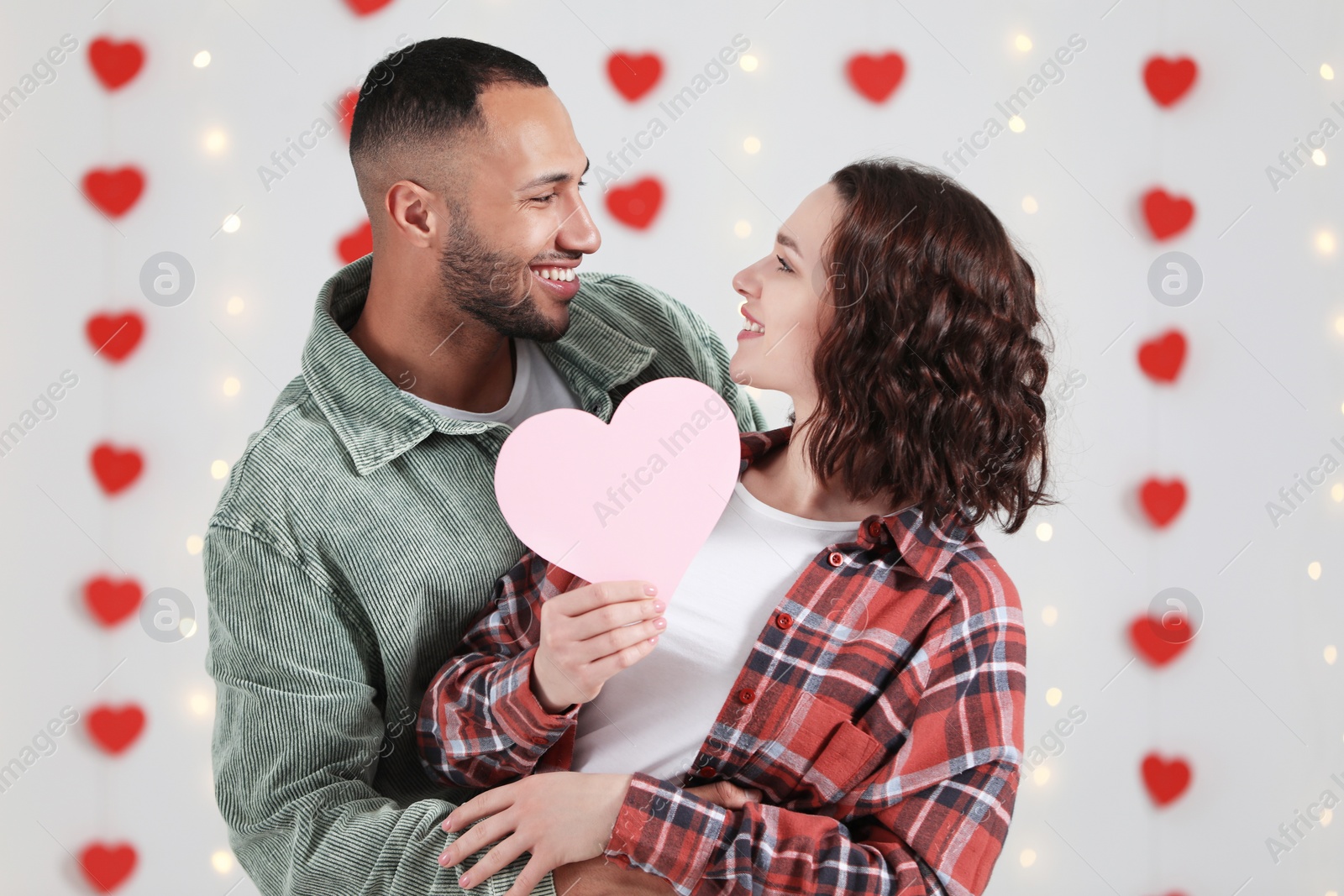Photo of Lovely couple with pink paper heart indoors. Valentine's day celebration