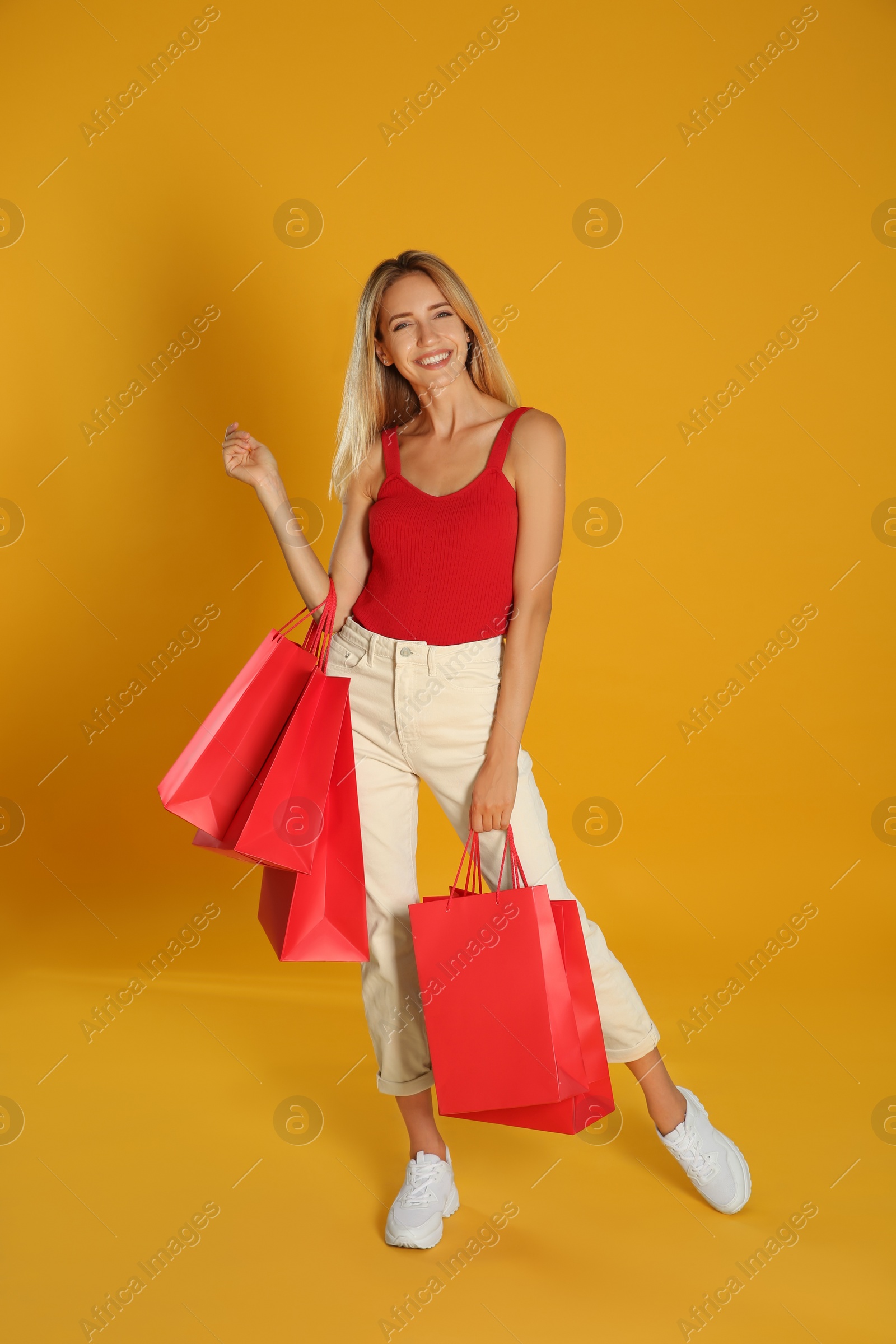 Photo of Happy young woman with shopping bags on yellow background. Black Friday Sale