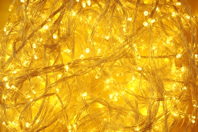 Photo of Glowing Christmas lights on yellow background, top view