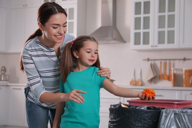 Photo of Little girl throwing tangerine peel into trash bin in kitchen. Separate waste collection