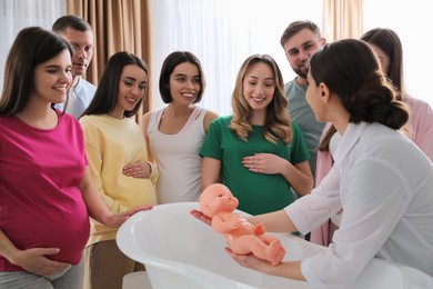 Pregnant women with men learning how to bathe baby at courses for expectant parents indoors