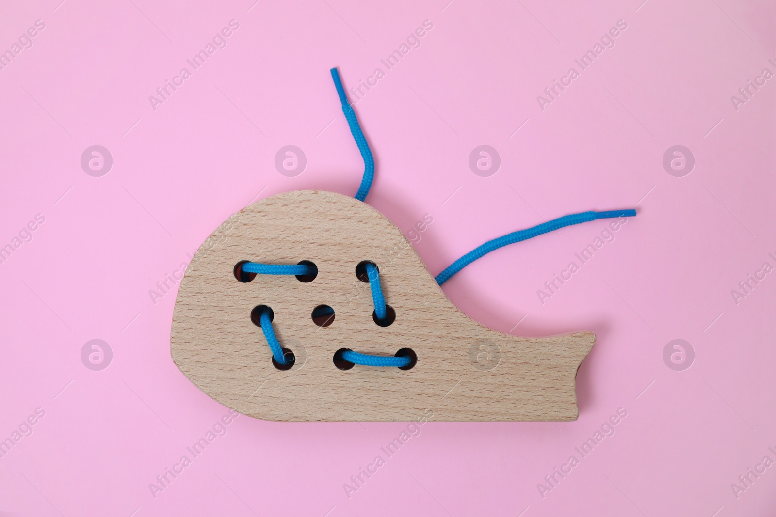 Photo of Wooden whale figure with holes and lace on pink background, top view. Educational toy for motor skills development
