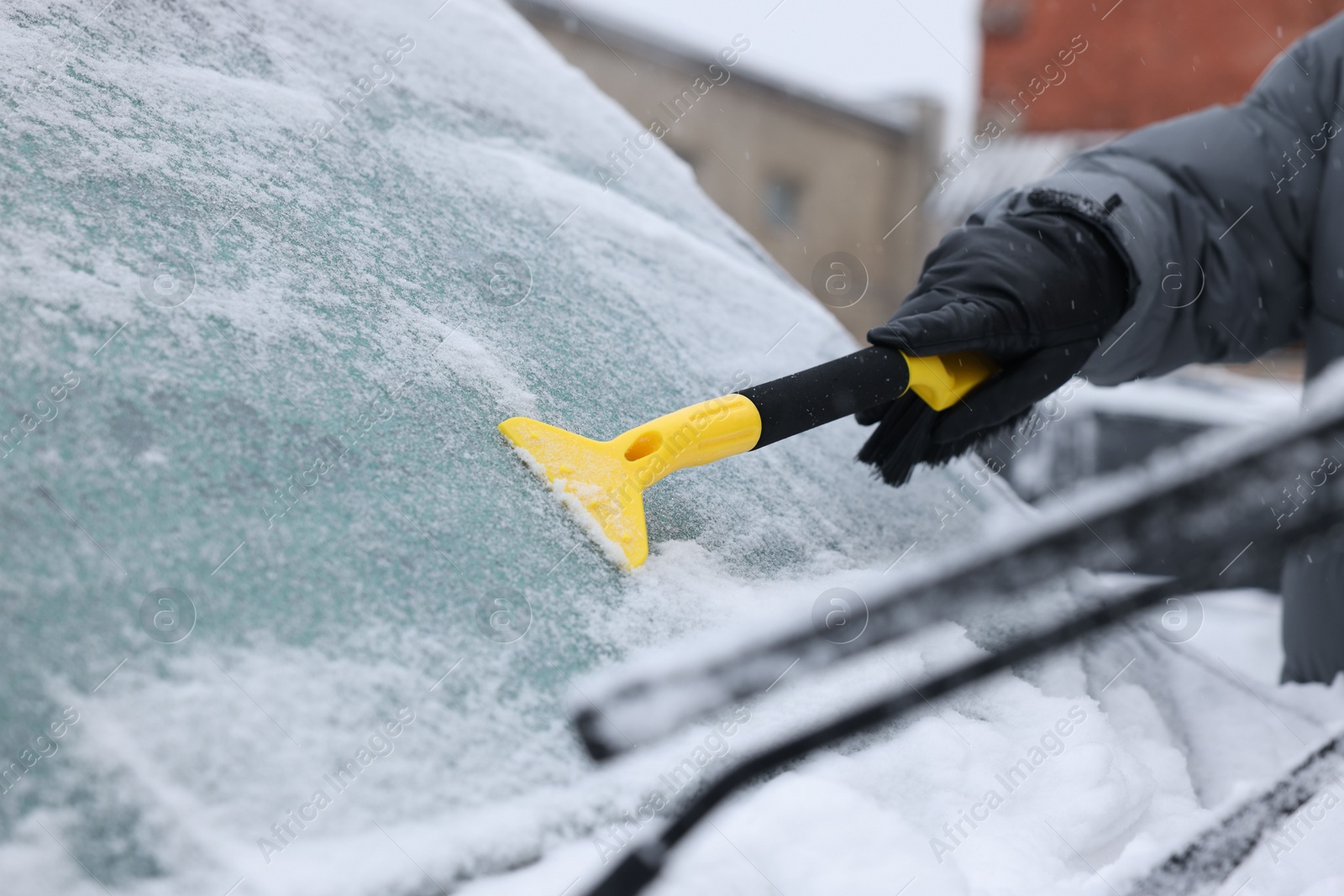 Photo of Man cleaning snow from car windshield outdoors, closeup