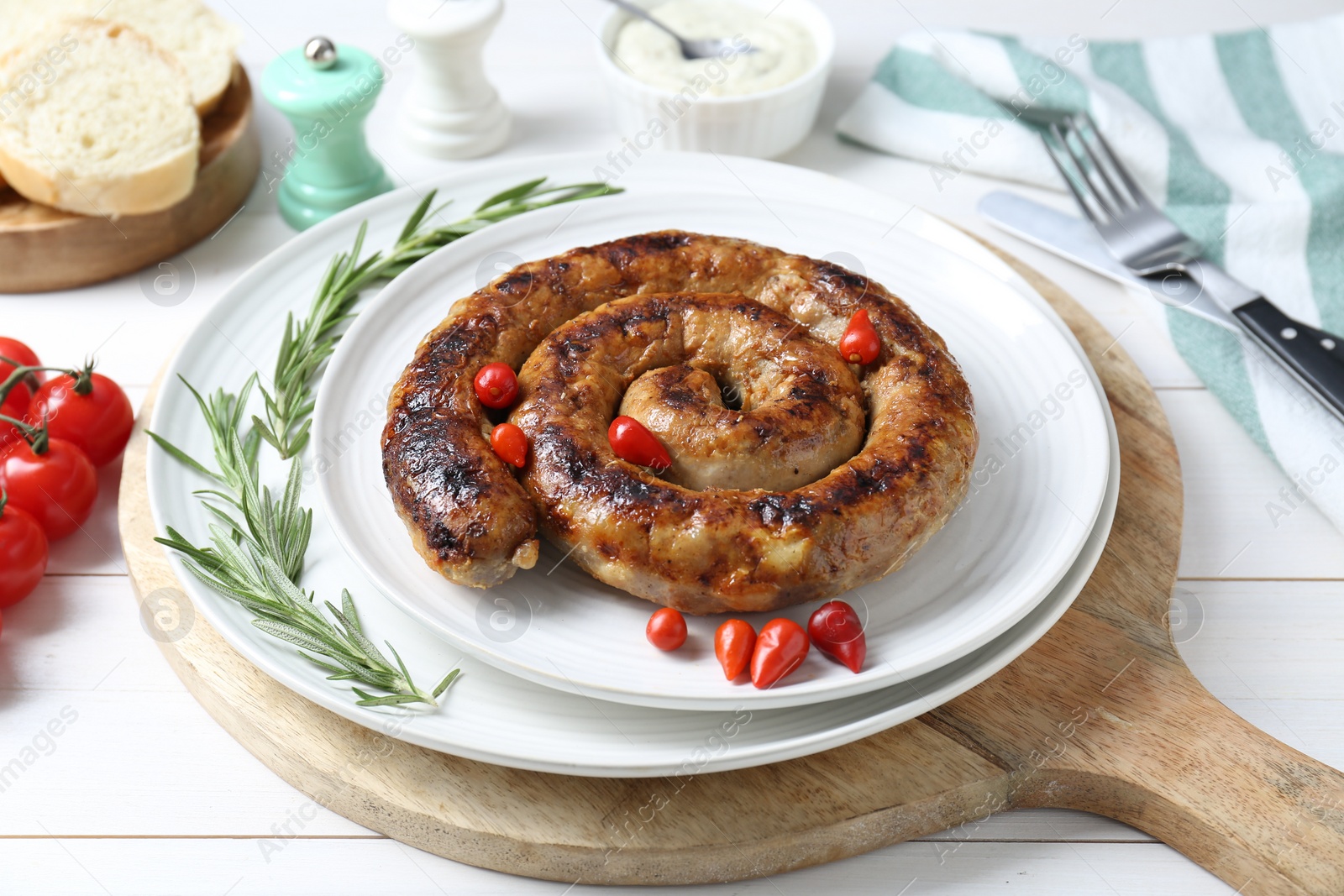 Photo of Tasty homemade sausages with peppers and rosemary on white wooden table