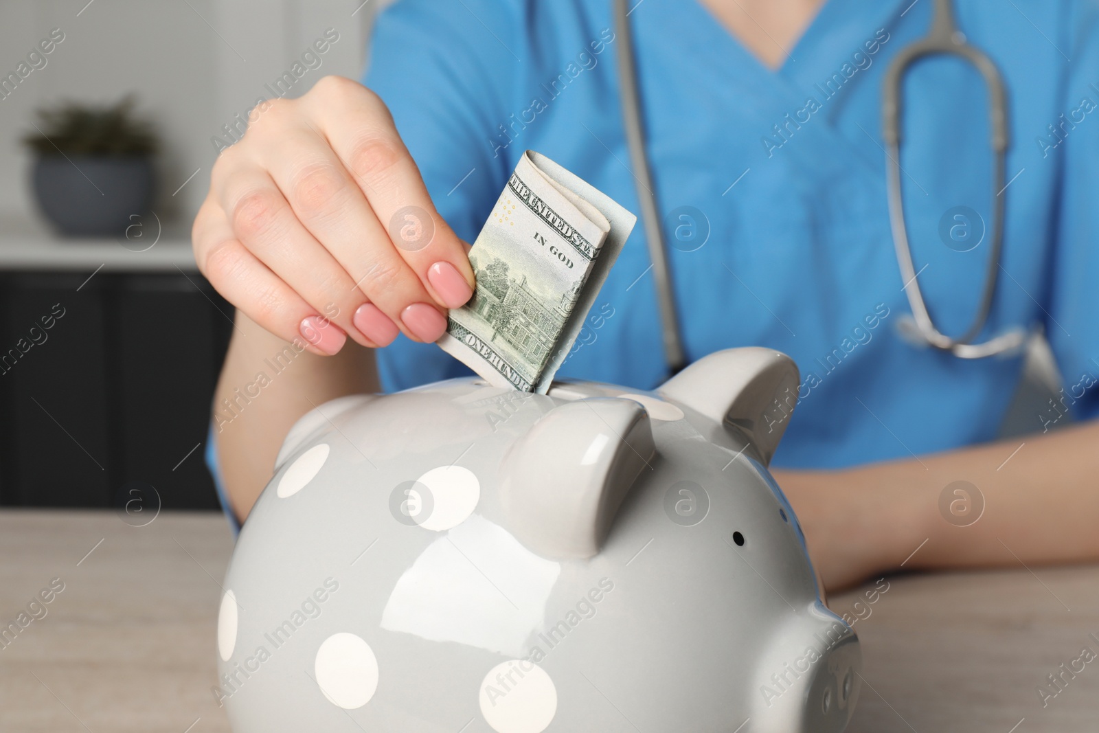 Photo of Doctor putting banknote into piggy bank at wooden table in hospital, closeup. Medical insurance