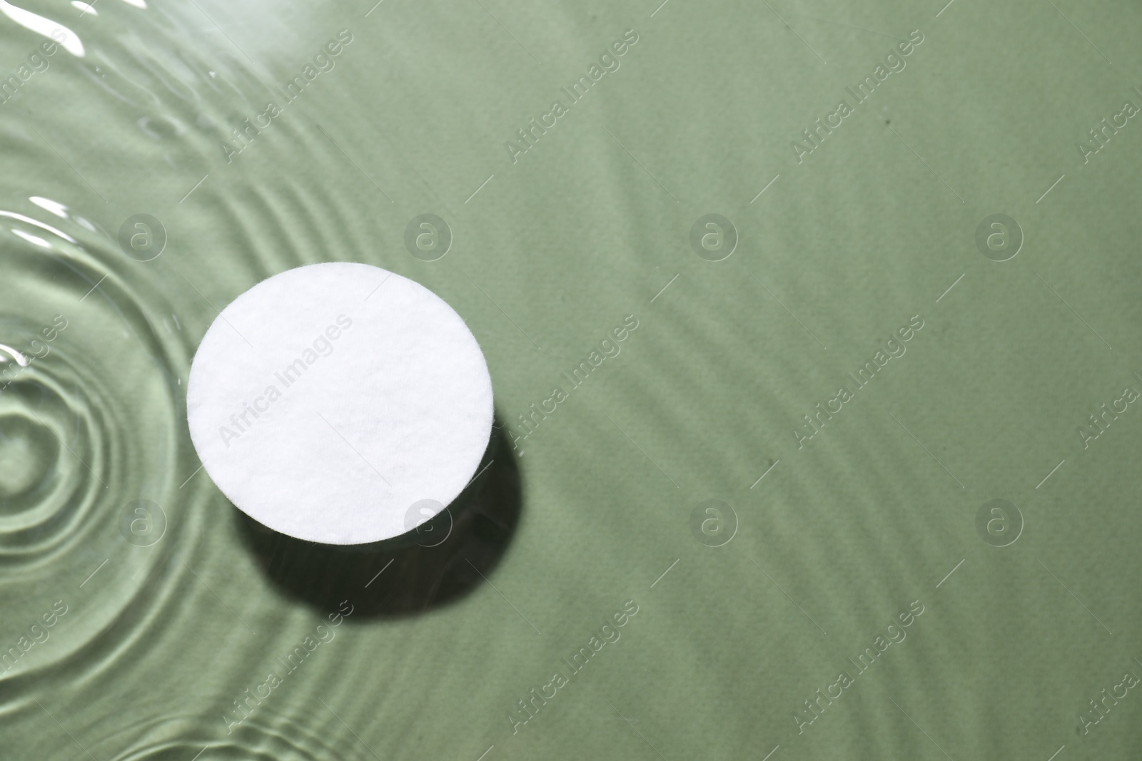 Photo of Cotton pad in micellar water on olive background, top view. Space for text