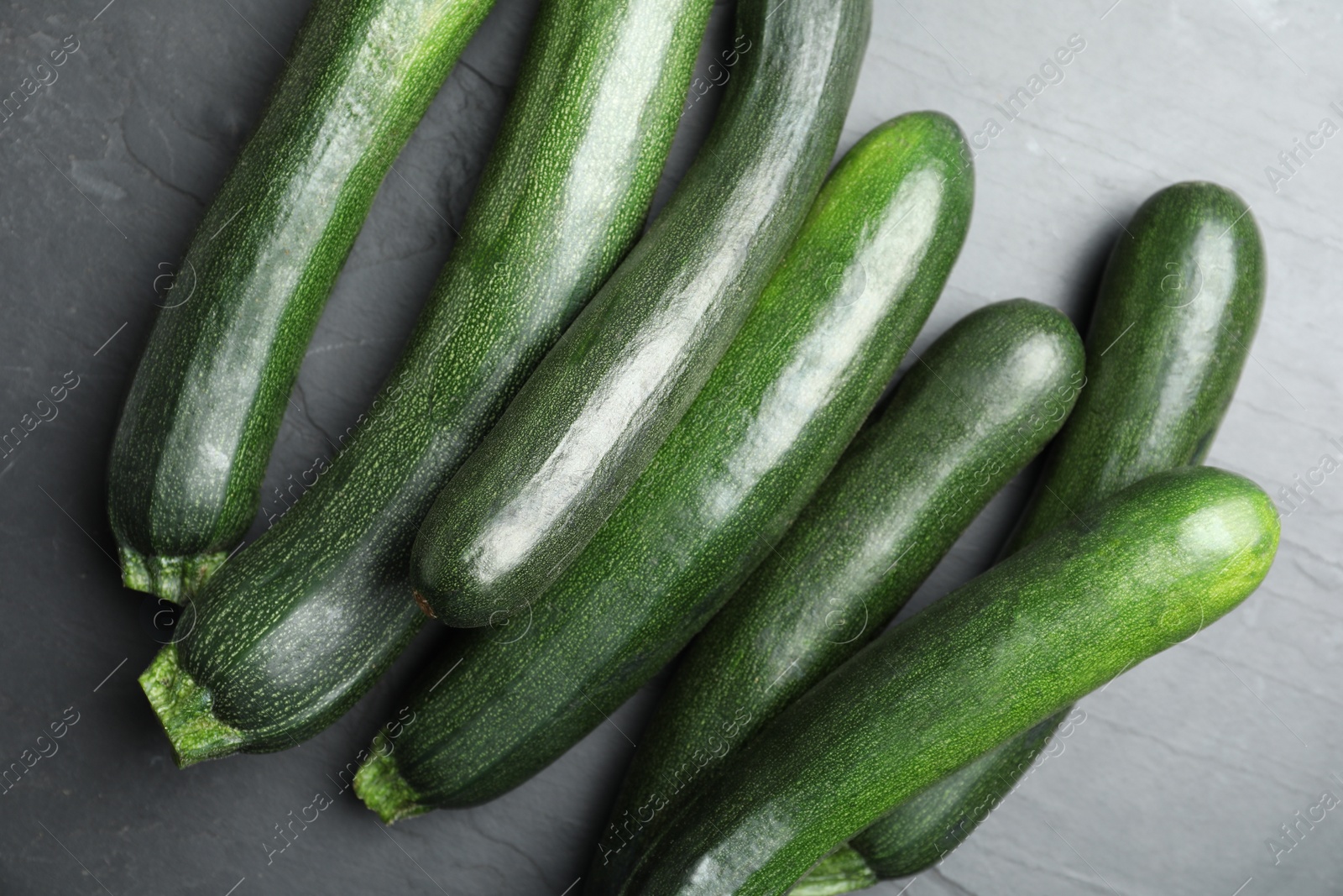 Photo of Green ripe zucchinis on black slate table, flat lay