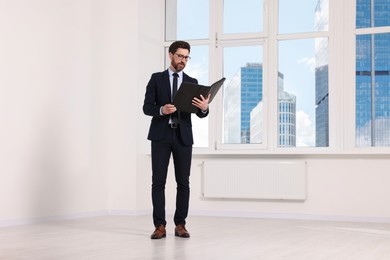 Handsome real estate agent with documents in empty room, space for text