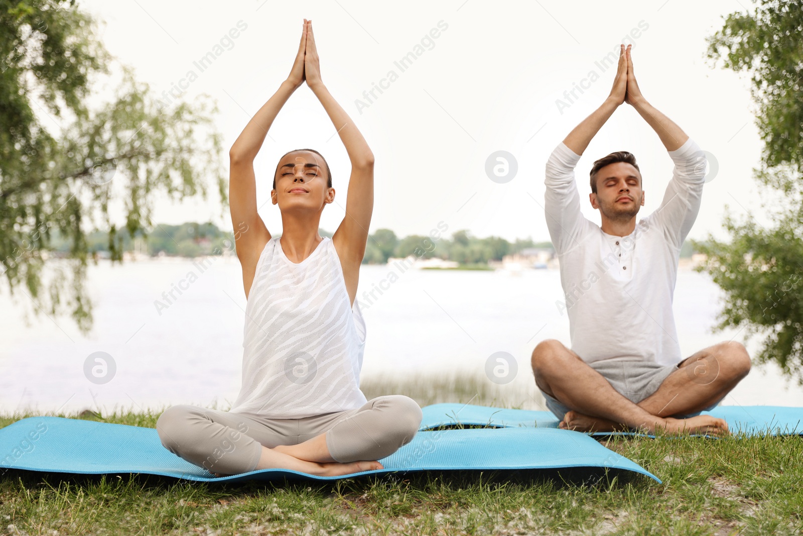Photo of Young couple practicing yoga in park near lake at morning
