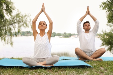 Young couple practicing yoga in park near lake at morning