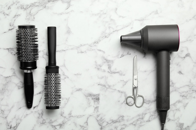 Photo of Hair dryer and professional hairdresser tools on white marble table, flat lay